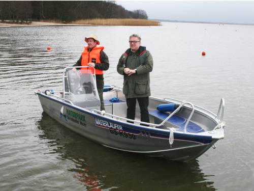 In einem Boot mit einem Rumpf aus korrosionsbeständigem Aluminium stehen zwei Männer und blicken in Richtung Ufer.